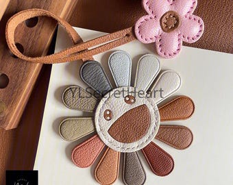 May include: A brown leather flower-shaped keychain with a smiling face and a pink flower charm attached to a brown leather strap.