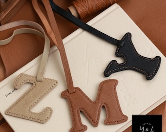 May include: Three leather keychains with different letter charms. The charms are in the shape of the letters Z, M, and Y. The Z charm is beige, the M charm is brown, and the Y charm is black.