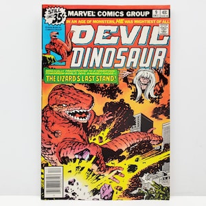 May include: A comic book cover featuring a red dinosaur with sharp teeth and claws, standing in a city with buildings in the background. The title of the comic is "Devil Dinosaur" and the text "In an age of monsters, he was mightiest of all" is printed above the title.