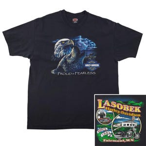 May include: Black Harley-Davidson t-shirt featuring a detailed graphic of an eagle with the text "PROUD & FEARLESS". The shirt also includes the Harley-Davidson logo and a smaller graphic with the text "LASOBEK Harley-Davidson" and "Fairmont, W.V."