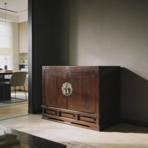 Puede incluir: Un mueble de madera marrón oscuro con dos puertas y un cierre metálico decorativo. El mueble tiene forma rectangular con tres pequeños cajones en la parte inferior. El mueble es un mueble.