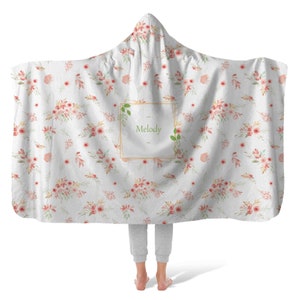 May include: A white hooded blanket with a floral pattern and a gold frame with the name "Melody" in green text.