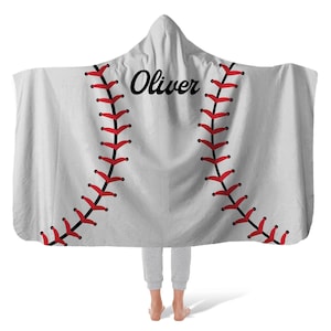 May include: A hooded blanket designed to resemble a baseball. The blanket is white with red stitching and the name "Oliver" in black script. The blanket is worn by a person.