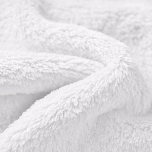 K&ouml;nnte beinhalten: Nahaufnahme eines wei&szlig;en, flauschigen Stoffes mit weicher, pl&uuml;schiger Textur. Der Stoff ist gefaltet und zerknittert, was ein Gef&uuml;hl von Komfort und W&auml;rme erzeugt.
