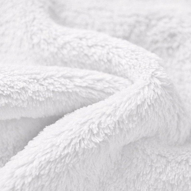 May include: Close-up of a white fluffy fabric with a soft, plush texture. The fabric is folded and wrinkled, creating a sense of comfort and warmth.