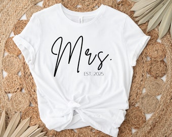 May include: White t-shirt with the text "Mrs. EST. 2025" in black script font.