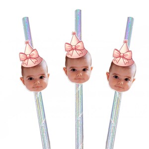 May include: Three iridescent straws with a pink bow and party hat on top of each straw. Each straw has a photo of a baby wearing a pink party hat with a bow on top.
