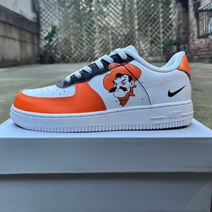 May include: White, orange, and black Nike Air Force 1 sneakers with a custom design featuring an orange and black mascot with a cowboy hat and the text "OSU".