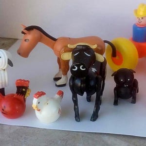 May include: A collection of colorful plastic farm animal toys, including a brown horse, black cow, sheep, two chickens, two dogs, and a tractor with a farmer figure. The toys are designed with simple shapes and bright colors.