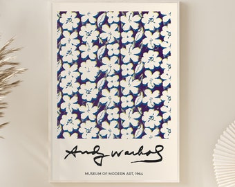 May include: A white framed print of a floral pattern in white and blue on a purple background. The print is signed "Andy Warhol" and includes the text "Museum of Modern Art, 1964". The print is hanging on a white wall above a white bench and a white wicker basket.