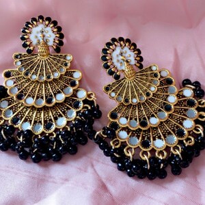 May include: A pair of gold-tone earrings with black beads and a layered design featuring white and silver accents.