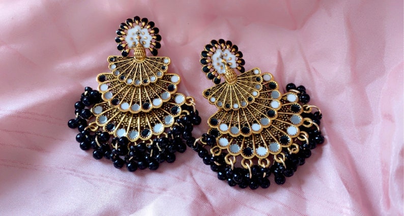 May include: A pair of gold-tone earrings with black beads and a layered design featuring white and silver accents.