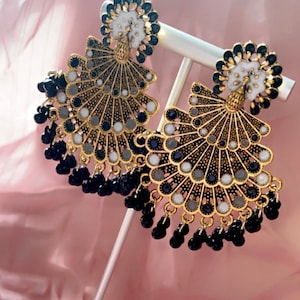 May include: A pair of gold-tone earrings with a peacock design. The earrings feature black and white beads and a fan-shaped design.