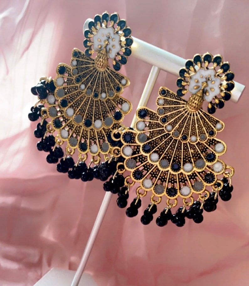 May include: A pair of gold-tone earrings with a peacock design. The earrings feature black and white beads and a fan-shaped design.