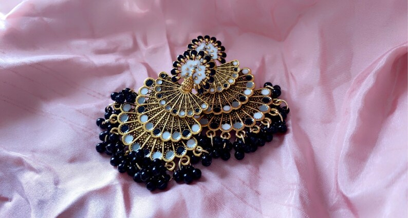 May include: A pair of gold tone earrings with black and white mirrored accents and black bead fringe.
