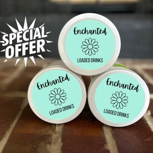 May include: Three white-lidded jars with turquoise labels are stacked. Each label features the word "Enchanted" in black script, a daisy graphic, and the words "LOADED DRINKS." The background is a textured, brown surface.