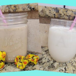 May include: Two drinks, one in a mason jar and the other in a stemless glass, each with a pink straw. The mason jar drink is light brown, and the glass drink is white. Three candies in yellow and orange wrappers are in front of the mason jar.