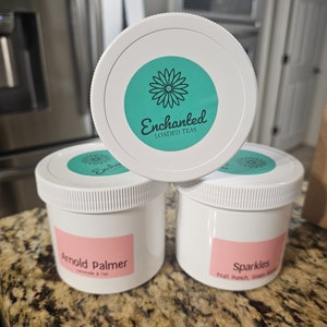 May include: Three white jars with pink labels and green lids. The labels read "Arnold Palmer Lemonade & Tea", "Sparkles Fruit Punch, Green Apple", and "Enchanted Loaded Teas".