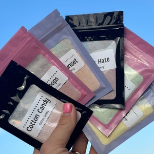 May include: Five small bags of bath salts with different scents and colors. The bags are labeled "Cotton Candy", "Pops", "Sunset", "Haze", and "Mango".