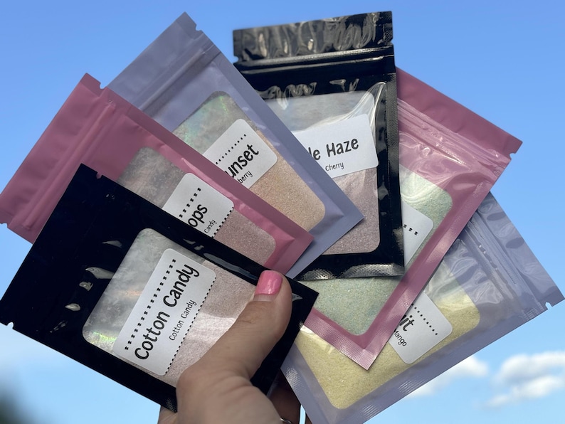 Puede incluir: Cinco peque&ntilde;as bolsas resellables llenas de purpurina iridiscente. Las bolsas est&aacute;n etiquetadas con los nombres "Cotton Candy", "Pops", "Sunset", "Purple Haze" y "Drift".