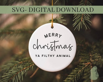Könnte beinhalten: Ein weißer Keramik-Weihnachtsschmuck mit dem Text "Merry Christmas Ya Filthy Animal" in schwarzer Schrift. Der Schmuck hängt an einem goldenen Faden vor einem verschwommenen Hintergrund aus grünen Tannennadeln. Oben im Bild steht "SVG- DIGITAL DOWNLOAD".
