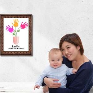 May include: A framed print with a handprint flower design. The print says "Auntie, I love you a bunch!" A woman is holding a baby in her arms.
