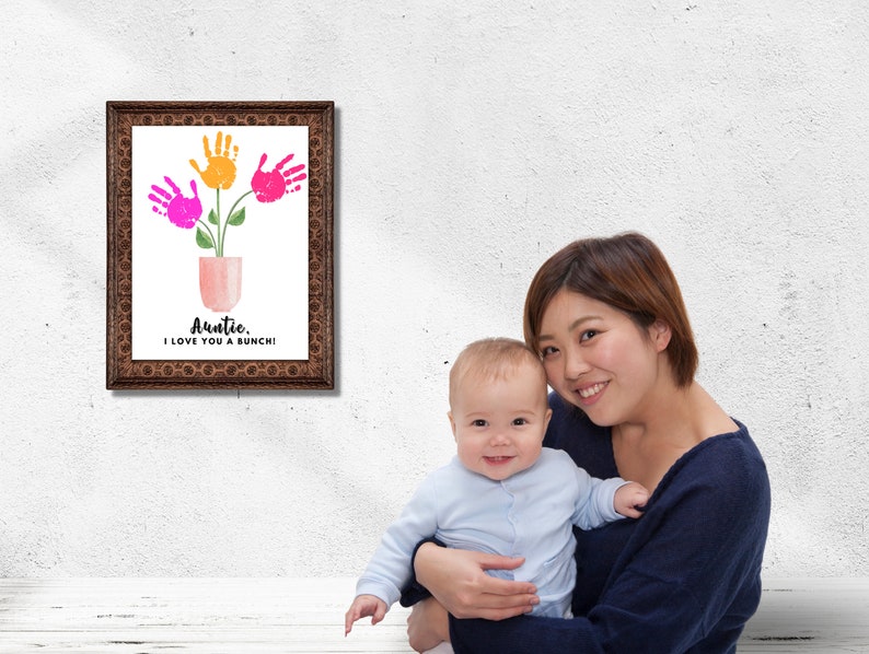 May include: A framed print with a handprint flower design. The print says "Auntie, I love you a bunch!" A woman is holding a baby in her arms.
