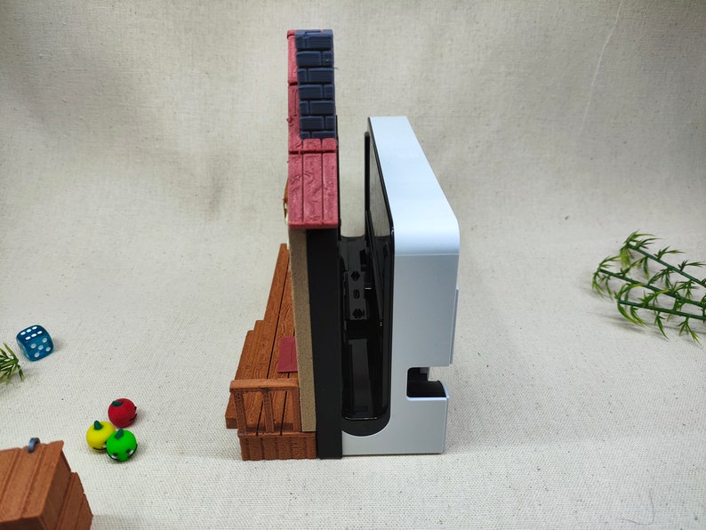 May include: A white and black video game console with a red, white, and brown miniature building attached to the side.