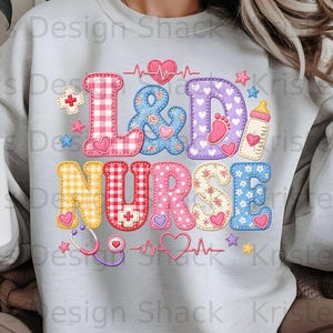 Puede incluir: Una sudadera de cuello redondo gris claro con un gráfico colorido en el pecho con el texto L&D NURSE. Las letras están decoradas con patrones de cuadros vichy, flores y lunares, acentuadas por corazones, un biberón y un estetoscopio.