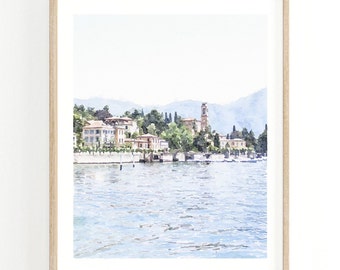 Peut inclure: Une peinture à l'aquarelle d'une ville sur un lac. La ville est construite à flanc de colline avec un clocher au centre. Le lac est d'un bleu clair et le ciel est d'un bleu clair. La peinture est encadrée dans un cadre en bois clair.
