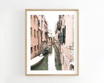 以下が含まれることがあります： イタリアのヴェネツィアの狭い運河の水彩画。運河はピンクの建物に囲まれ、水にはゴンドラが2隻あります。