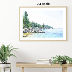 May include: A watercolor painting of a lake scene with a shoreline of trees and rocks. The water is a light blue color and the sky is a light blue color. The painting is framed in a light wood frame.