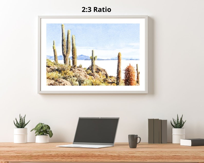 May include: A watercolor painting of a desert landscape with tall cacti and a body of water in the background. The sky is a light blue with white clouds. The painting is framed in a white frame.