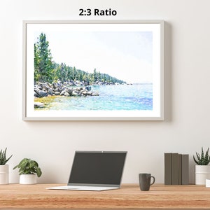 May include: A watercolor painting of a lake scene with a shoreline of trees and rocks. The water is a light blue and the sky is a light blue with white clouds. The painting is framed in a white frame.