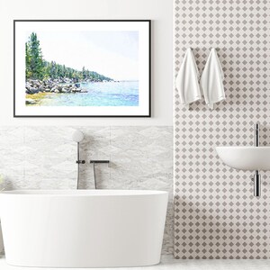 May include: A white bathtub with a black faucet and shower head in a bathroom with a white tiled wall and a framed watercolor painting of a lake and trees.