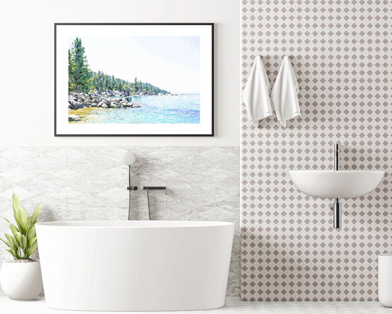 May include: A white bathtub with a black faucet and shower head in a bathroom with a white tiled wall and a framed watercolor painting of a lake and trees.
