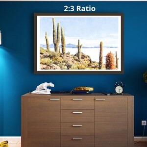 May include: A framed watercolor painting of a desert landscape with tall cacti and a distant lake. The painting is titled "2:3 Ratio" and is displayed on a wall.