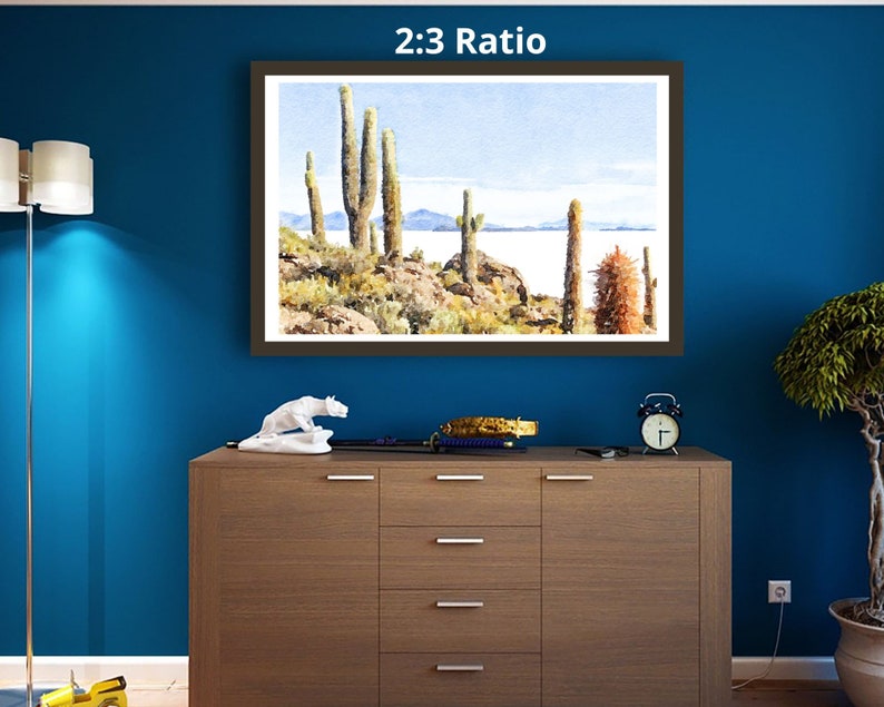 May include: A framed watercolor painting of a desert landscape with tall cacti and a distant lake. The painting is titled "2:3 Ratio" and is displayed on a wall.
