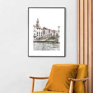 Puede incluir: Una impresi&oacute;n en acuarela enmarcada de un puente veneciano sobre un canal. La obra de arte presenta una representaci&oacute;n detallada del puente con edificios y una torre al fondo. La impresi&oacute;n est&aacute; en un marco negro y cuelga de una pared blanca.