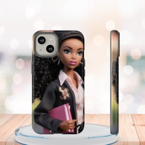 May include: A phone case featuring a doll dressed in a black blazer, pink shirt, and holding a pink notebook. The doll has dark skin, blue eyes, and curly black hair. The case is shown from the front and side.