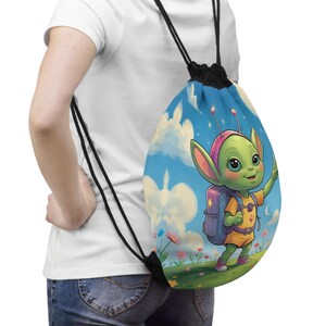May include: A drawstring backpack featuring a cartoon alien character with a backpack, set against a blue sky with clouds and flowers. The alien is green with large eyes and wearing a pink headband and orange shirt.