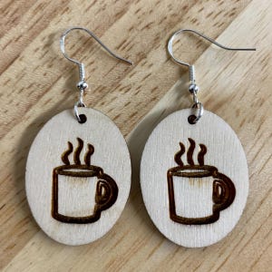 May include: A pair of wooden earrings with a coffee cup design. The earrings are oval shaped and have silver hooks.