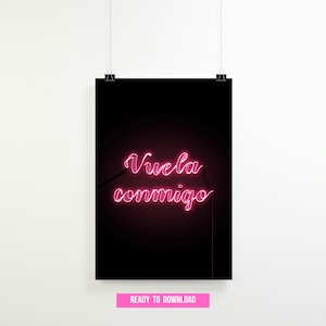Könnte beinhalten: Ein schwarzes Poster mit dem neonrosa Text "Vuela conmigo" (Flieg mit mir). Der Text ist in einer Schreibschrift. Das Poster hängt an einer weißen Wand.