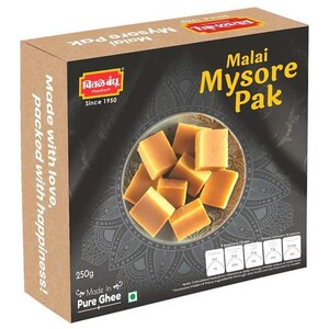 May include: A box of Malai Mysore Pak, a traditional Indian sweet made with ghee. The box is brown with a black and white design and features a picture of the sweet on the front. The text on the box reads "Malai Mysore Pak" and "Made with love, packed with happiness!"