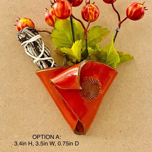 May include: A red ceramic wall planter with a swirl design, holding a small bouquet of faux red berries and green leaves. The planter is 3.4 inches high, 3.5 inches wide, and 0.75 inches deep. OPTION A: 3.4in H, 3.5in W, 0.75in D