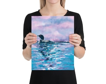 May include: A black and white loon with red eyes swims in a blue and purple lake with a pink and purple cloudy sky in the background.