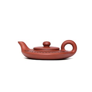 May include: A red clay teapot with a round lid and a curved handle. The teapot features an intricate design with detailed carvings.
