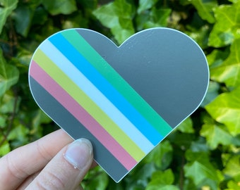 Puede incluir: Una pegatina en forma de corazón con un diseño de rayas diagonales en rosa, amarillo, blanco, azul y verde. La pegatina está sobre un fondo gris oscuro.