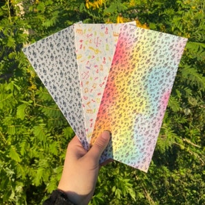 May include: Three different patterned sheets of paper with musical notes printed on them. The sheets are white with black musical notes and have a rainbow gradient, a black and white pattern, and a white pattern with colorful musical notes.
