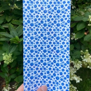 Puede incluir: Una hoja de tela blanca con un patrón floral azul. La tela está impresa con pequeñas flores azules y tallos.